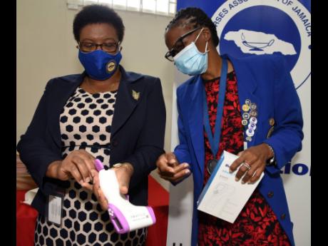 Carmen Johnson (right), president of the Nurses Association of Jamaica 
and Patricia Ingram-Martin (left), chief nursing officer, Ministry of Health and Wellness, check the batteries of one of the 200 infrared thermometers and 200 face masks they received 