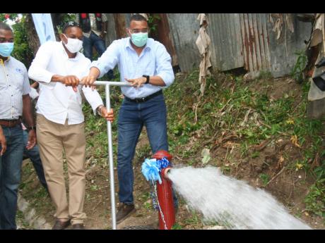 Prime Minister Andrew Holness (right) is assisted by Hanover Eastern Member of Parliament Dave Brown in opening the valve to allow water to flow through a hydrant in the community of Claremont during the commissioning of the Claremont-to-Jericho water-supp