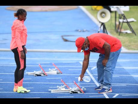 Megan Tapper (left) looks on while a meet official sprays the blocks before her 100m hurdles race at the Velocity Track meet held at the National Stadium recently.