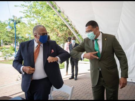 Jamaica Labour Party (JLP) Leader Andrew Holness (right) and People’s National Party (PNP) President Dr Peter Phillips elbow-greet while playfully displaying political symbols at the signing of the Political Code of Conduct at Emancipation Park in New Ki