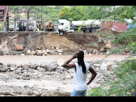 Junior Gayle looks on at a truck trailer with one wheel hanging precariously over the bank of the Cane River in Eight Miles, Bull Bay, on Monday, a day after eastern Jamaica was walloped by the flood rains of Tropical Storm Laura.