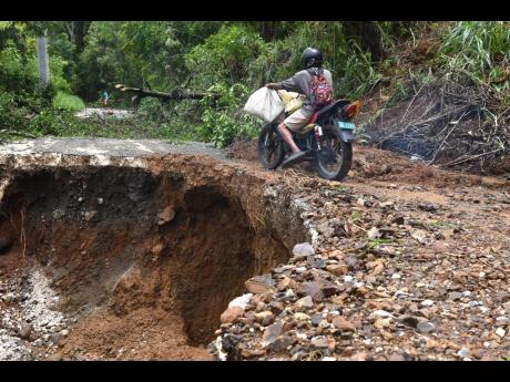 A motorcyclist inches his way along a section of the Cedar Valley main road in St Thomas which collapsed, leaving many residents stranded on Monday. Some communities are currently without electricity after storm rains damaged road and other infrastructure.