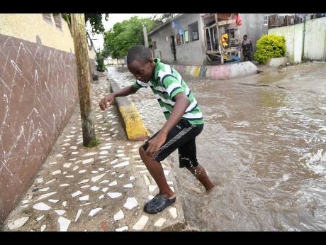 A boy crossing a section of the flooded White Lane yesterday in Waterhouse, St Andrew. The roadway looks like a part of the official drainage network whenever it rains in Waterhouse, St Andrew.