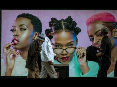 Men in face masks walk past a hair product billboard on the street in Soweto, South Africa. The coronavirus pandemic has fractured global relationships as governments act in the interest of their citizens first, but John Nkengasong, Africa’s top public h