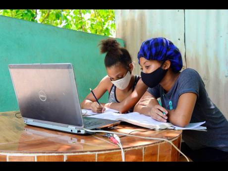 
Two students of The Queen’s School accessing classes using a laptop under an ackee tree on Mountain View Avenue in Kingston last Wednesday. One of the girls had slept over at her classmate’s house so they could have classes together.