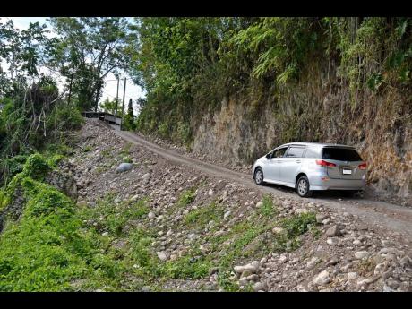 A motorcar along the ‘Bruk Weh’ road, with piece of the wall that collapsed years ago at left.