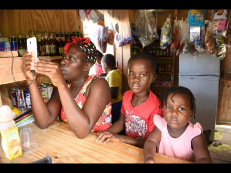 Alicia Morand tries to pick up a signal alongside son Ajani Wood and daughter Ajanique Young in Morand’s shop. Residents of Epsom, St Mary, have lamented connectivity woes that are affecting online classes.