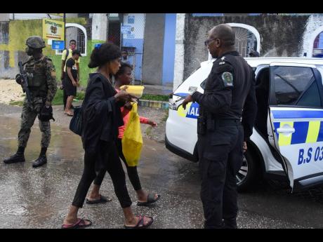 Assistant Superintendent Andrew Johnson looks on as 14-year-old Mikayla Anderson of Waterhouse in St Andrew is escorted to a police vehicle after being rescued by residents from floodwaters in the Sandy Gully yesterday. She had sought refuge on a concrete 