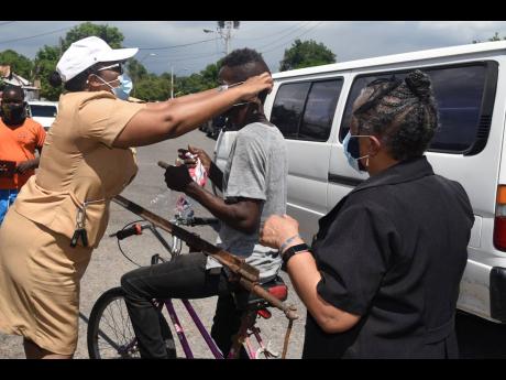 Senior Public Health Nurse Charmaine Vassell-Shettlewood puts on a mask on a pedal cyclist along Waltham Park Road in St Andrew on Wednesday while Dr Audre McIntosh from the Ministry of Health looks on.