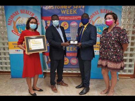 Chief executive officer of the National Health Fund (NHF), Everton Anderson (second left), along with director of health promotion public relations and customer care, Shermaine Robotham (left), collects the trophy and certificate from deputy chairman of th