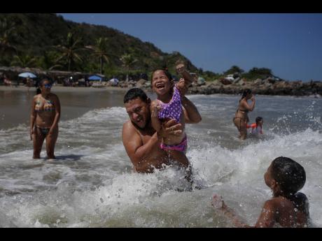 Caracas resident Jose Velasco lifts his daughter, Ashley Velasco, above a wave off La Ultima beach after it recently reopened following a lockdown to contain the spread of COVID-19 in La Guaira, Venezuela, on Friday.