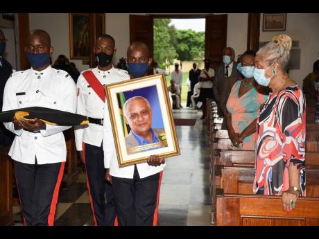 Police Sergeant Kevin Wallace (second right) marches past Beverley Anderson Duncan (right), widow of Dr D.K. Duncan, with his photograph during the funeral at the University Chapel in Mona, St Andrew, on Sunday. Also marching are trainee constables André 