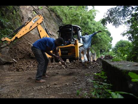 A man, with the help of a tractor, clears a land slippage that blocked the Mount Felix main road in St Thomas on Monday after heavy rains battered the island on the weekend. 
