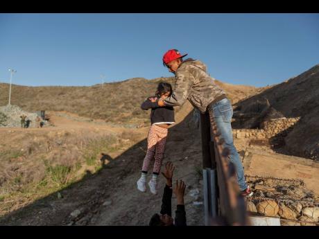 AP 
In this January 3, 2019 file photo, a migrant from Honduras passes a child to her father after he jumped the border fence to get to the United States side to San Diego, California, from Tijuana, Mexico. Hondurans are expected to send US$2.5 billion bac