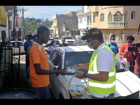 Health Minister Dr Christopher Tufton (right) hands out packets of face-masks to a resident of Cornwall Courts in St James during a walk-through of the community on Friday. Cornwall Courts has been under a special curfew since October 23, following an inc