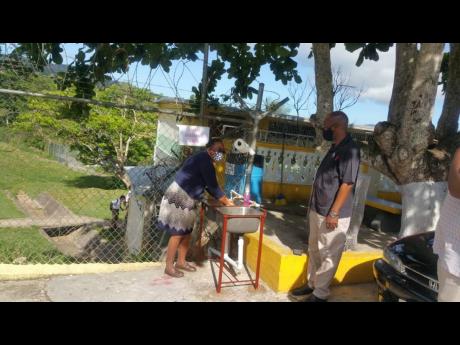 Alston High Vice-Principal Murdina Latty-Johnson uses a handwashing station set up at the school while Principal Adrian Sinclair looks on.