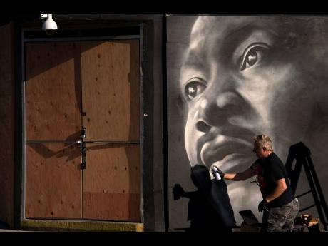 Artist Shane Grammar paints a portrait of Martin Luther King Jr Monday on the sheets of plywood outside a boarded-up jewellery shop in Los Angeles amid worries about potential demonstrations and violent responses to today’s general election.