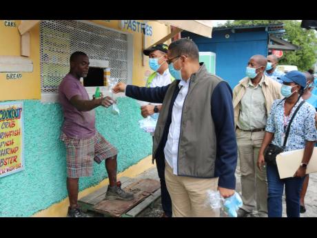 Health and Wellness Minister Dr Christopher Tufton looks on as a customer accepts a mask from Kingston Central Member of Parliament Donovan Williams during a tour of Rae Town on Wednesday. The community has been placed under a special COVID curfew since Oc