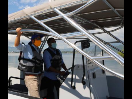 Jamaica's resident representative to the World Bank, Ozan Sevimbli (left), looks on as Minister of Agriculture and Fisheries Floyd Green checks out the controls of the new boat presented to the National FIsheries Authority recently. 