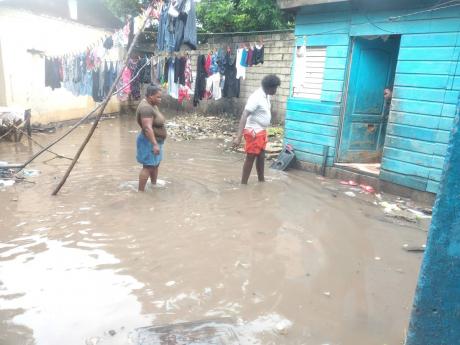Residents plod through floodwaters in a yard situated on of Olympic Way, St Andrew, on Sunday. As heavy rainfall associated with Tropical Storm Eta triggered landslides and flooding across Jamaica, the Meteorological Service announced a flash flood warning