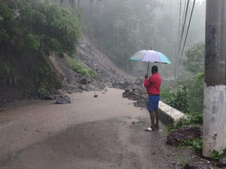 A man observes the effects of a landslide along the Gordon Town main road in St Andrew on Sunday. More rains are forecast for today. 