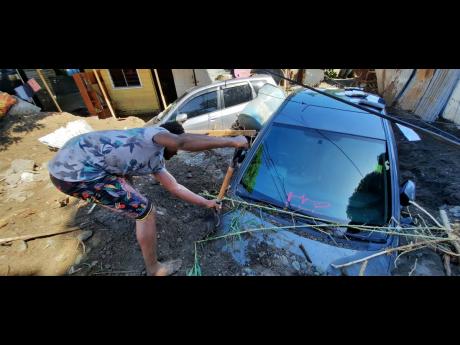 Kemar King shovels away sand and stones that submerged his sister’s cars in Nine Miles, St Andrew, on Monday after the Chalky River dumped tons of silt on the rain-ravaged community on the weekend. 