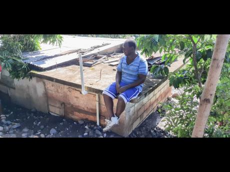 Fitzgerald Benjamin sits atop his 12ft-high roof after his yard was swamped with silt after the Chalky River broke its banks on the weekend. 
