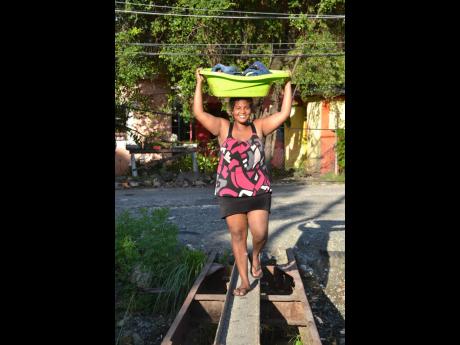 A resident balances a wash basin filled with clothes as she walks across a narrow footbridge in Bambo River, St Thomas, on Monday. The eastern Jamaica community was hit  by flood rains on Sunday. 