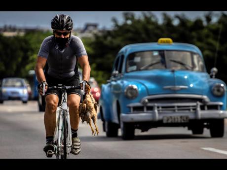 A cyclist wearing a mask as a precaution against the spread of the coronavirus carries a chicken in his hand while he pedals his bicycle in Havana, Cuba, on October 11, 2020. There are hopes for a warming of relations between Cuba and the United States as 