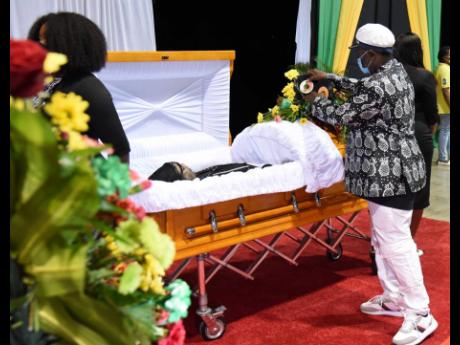 Herman Davis, popularly called ‘Bongo Herman’, prepares to place a 45 record in the casket of Frederick ‘Toots’ Hibbert, while the body of the legendary musician was being viewed by members of the public yesterday at the National Indoor Sports Comp