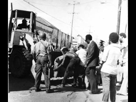 In this November 1980 file photo, National Security Minister Winston Spaulding (third right) oversees the clearing of a road block on Gold Street in Central Kingston in the aftermath of the bloody 1980 general election campaign. A policeman (left) carries 