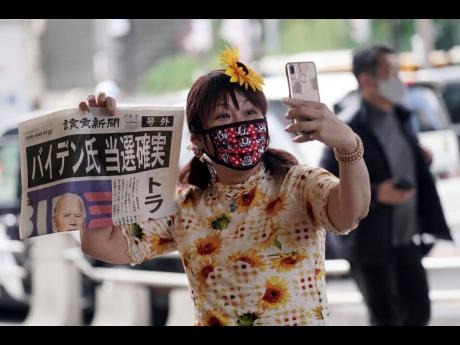 A passer-by takes a selfie with an extra newspaper reporting on President-elect Joe Biden’s win in the U.S. presidential election, in Tokyo. The headline reads: “Mr. Biden assured of win.”