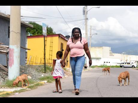 Faye Grant walks with her granddaughter along the streets of Trench Town, St Andrew, accompanied by three dogs she boasts as their bodyguards. 