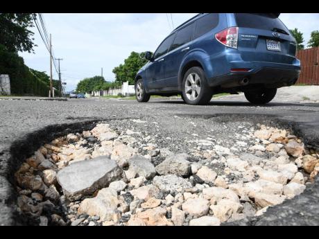 A motorist drives past a pothole on Elizabeth Avenue, off Red Hills Road, in St Andrew on Sunday. Dozens of roads across Jamaica have been damaged by tropical storms Eta and Zeta. 