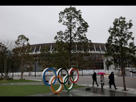 People walk past the Olympic rings near the New National Stadium in Tokyo, Wednesday, March 4, 2020. 
