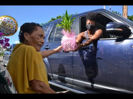 A gift-giver hands a present to Curline Lyon during a drive-through birthday celebration outside her Kingston home on Saturday. Lyon, whose family raves about her "legendary dumplings", turns 100 today, coming full circle to survive two of the most deadly 