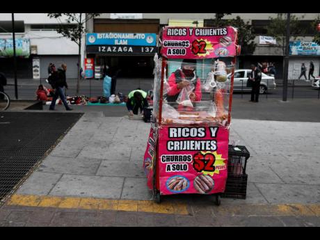 A vendor, wearing a protective face mask, is bundled up against the cold as she prepares churros in her mobile stall in Mexico City, Wednesday, November 18, 2020, amid the new cornavirus pandemic.