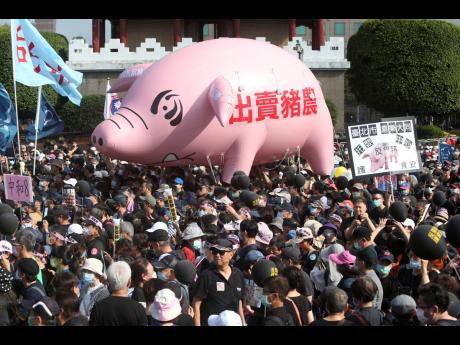 People hold the model of a  pig marked with the slogan ‘Betraying pig farmers’ during a protest in Taipei, Taiwan, on Sunday, November 22. 