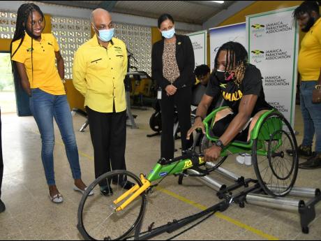 Para-athlete Kino Hewitt demonstrates the use of the wheelchair roller to (from left) athlete Shauna Kay Hones, Jamaica Paralympic Association President Christopher Samuda and CHASE Fund Project Manager Latoya Aquart-Forrest  at the Sir John Golding Rehab 
