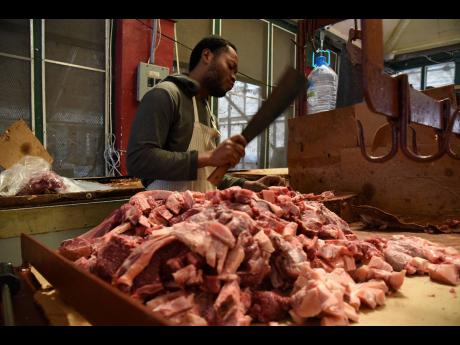 Rushon Grey cuts up pork for his customers inside the Spanish Town market on Tuesday. Meat shop operators in the Old Capital are fearful that there will be below-normal supplies of pork for Christmas. 