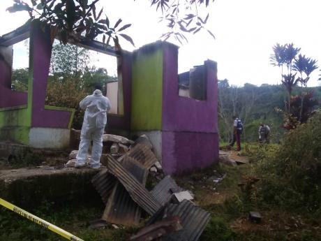 Police personnel processing the scene at a burnt-out house in Wait-A-Bit, Trelawny, where the charred remains of two men, believed to be brothers, were discovered last Friday.
