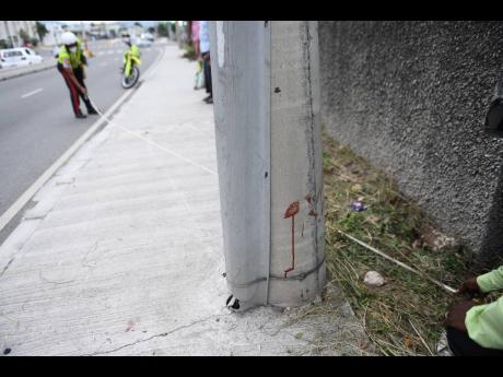 Blood spatter serves as a grim reminder of a crash scene as a policeman takes measurements on Constant Spring Road, St Andrew, on Thursday. A motorcyclist lost control of his bike after colliding with a motor car, sending him and a pillion passenger crashi