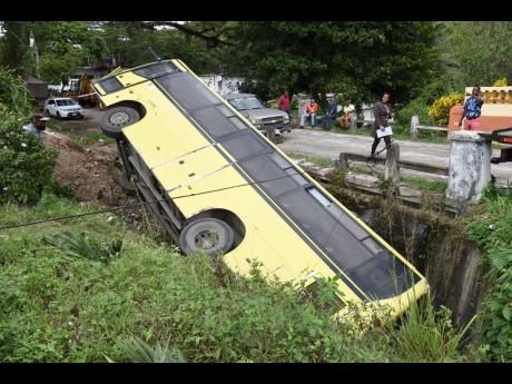 A Jamaica Urban Transit Company bus lying in a ditch in Temple Hall, St Andrew, yesterday after reportedly hitting a parked wrecker. The injured driver, who was the sole occupant, was rushed to hospital.