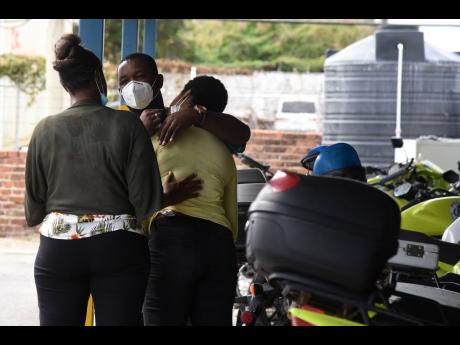 A police officer consoles a relative of Constable Fabian Morrison at the Elletson Road Police Station yesterday. Morrison died after being hit from a motorcycle along Camp Road in Kingston yesterday.