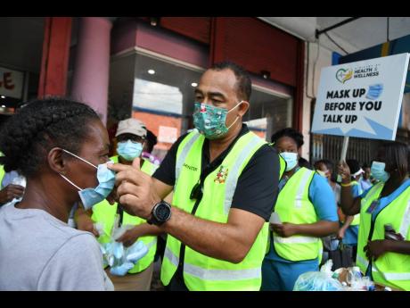 Minister of Health and Wellness Dr Christopher Tufton fits a mask on Beverlyn Burgess' face during a sensitisation event in downtown Kingston on Thursday, December 10, during which masks and hand sanitiser were distributed. 