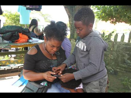 Seven-year-old Jayden McNaught assists Nordia Francis to connect to the free public Wi-Fi installed in Chapelton by the Universal Service Fund.