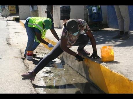 Councillor for the Lucea division in the Hanover Municipal Corporation, Easton Edwards (left), and volunteer Marvia Brown  play their part in beautifying a curb wall along the main streetin  Lucea on Sunday, as part of a clean-up and beautification project