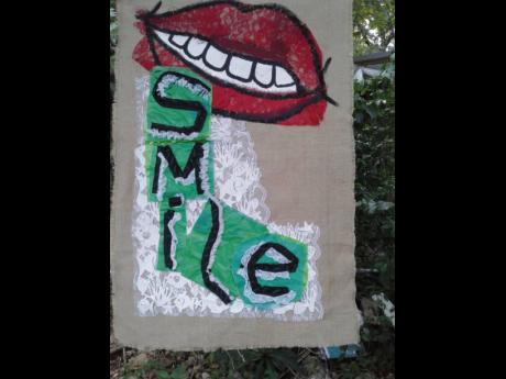 Artist Tukula Ntame’s banner invites you to smile. The banner is one of 16 works by local artists and artisans with positive words that hang along Oracabessa main street.   