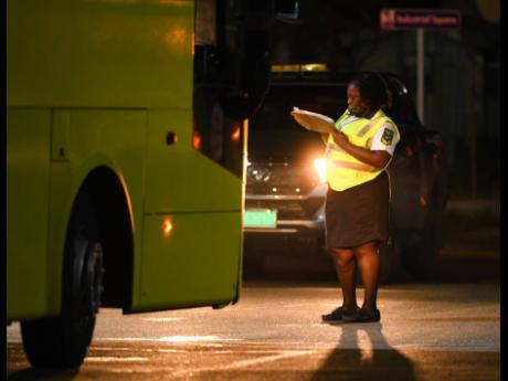 A security guard checks Jamaica Urban Transit Company buses entering a restricted area of the Norman Manley International Airport on Monday evening. The buses were deployed to transport passengers who came on a British Airways flight and will be taken into