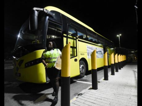 A security guard walks past one of several Jamaica Urban Transit Company buses deployed to transport travellers from the United Kingdom to quarantine in St Ann.